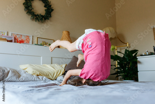 little girl in pink pajamas doing somersault on the bed