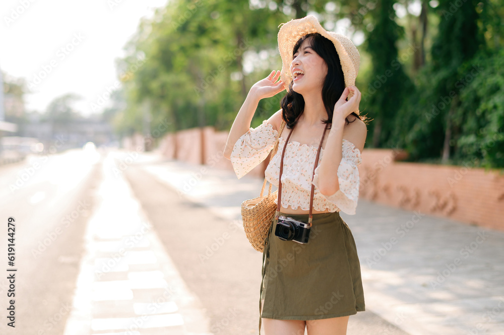 Portrait of asian young woman traveler with weaving hat and basket and a camera standing by the street. Journey trip lifestyle, world travel explorer or Asia summer tourism concept. Portrait of asian young woman traveler with weaving hat and basket and a camera standing by the street. Journey trip lifestyle, world travel explorer or Asia summer tourism concept.