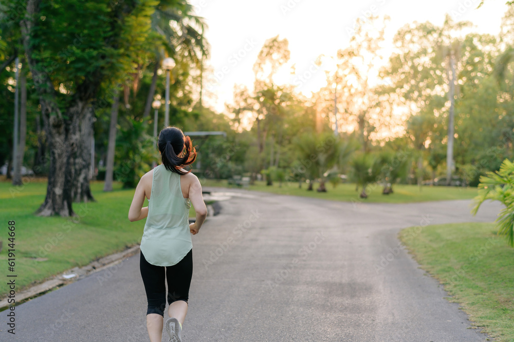 Obraz premium Fit Asian young woman jogging in park smiling happy running and enjoying a healthy outdoor lifestyle. Female jogger. Fitness runner girl in public park. healthy lifestyle and wellness being concept