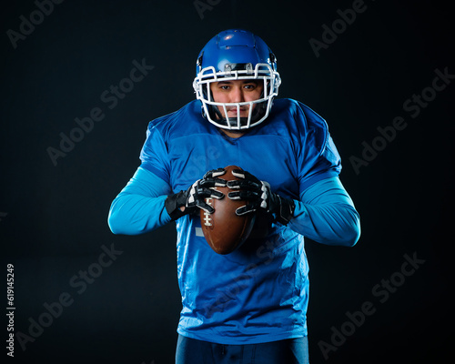 Portrait of a man in a blue uniform for american football on a black background.  © Михаил Решетников