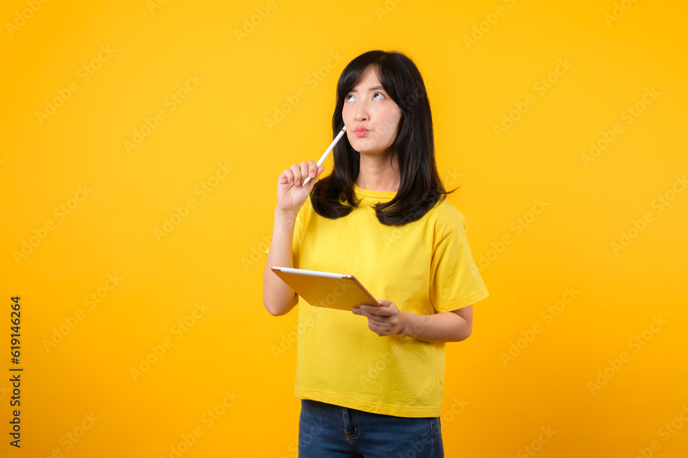 Experience range of emotions with portrait. A young Asian woman wearing yellow t-shirt and denim jeans showcases doubtful expression while using tablet. diverse emotions and technology usage concept. Experience range of emotions with portrait. A young Asian woman wearing yellow t-shirt and denim jeans showcases doubtful expression while using tablet. diverse emotions and technology usage concept.
