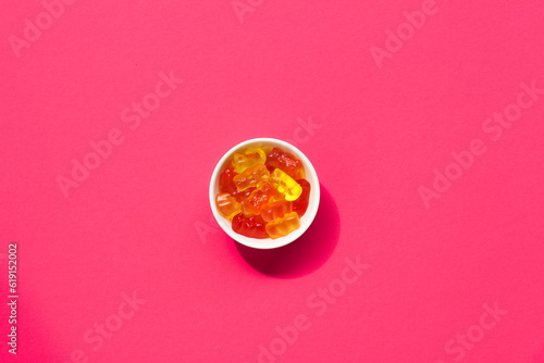 Healthy gummy red bears in white bowl on colorful background, light with shadow, copy space, background texture, legal cbd medical candy concept