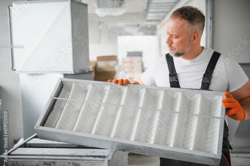 Canvas Print A male worker holds an air filter for air conditioning in an office space