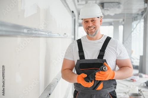 man drywall worker or plasterer putting mesh tape for plasterboard on a wall using a spatula and plaster. Wearing white hardhat, work gloves and safety glasses. Image with copy space. © Serhii