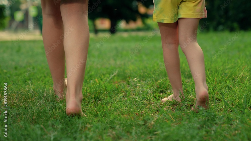 Bare feet mom, child, close-up go on green grass. Concept healthy lifestyle. Family walk barefoot on green lawn on sunny day. Barefoot mom, boy, girl go on green grass in park. Kid, mother fun outdoor