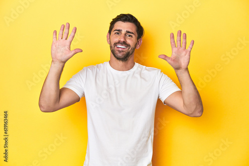 Caucasian man in white t-shirt on yellow studio background showing number ten with hands.