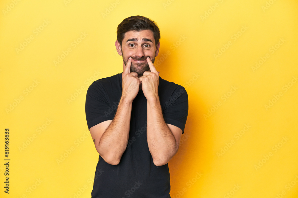 Caucasian man in black t-shirt, yellow studio backdrop doubting between two options. Caucasian man in black t-shirt, yellow studio backdrop doubting between two options.