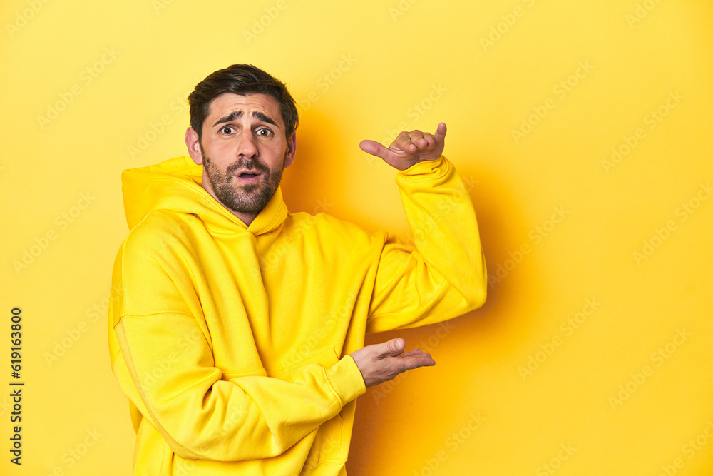 Obraz premium Man in yellow hoodie, monochrome studio backdrop shocked and amazed holding a copy space between hands.