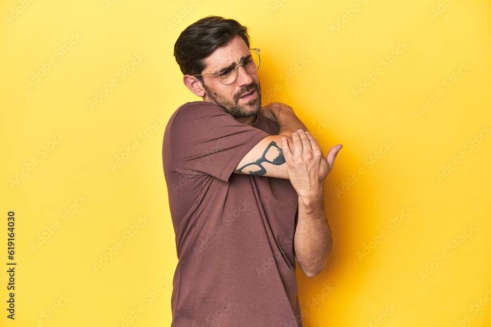 Man stretching arm on a yellow studio background. - obrazy, fototapety, plakaty 