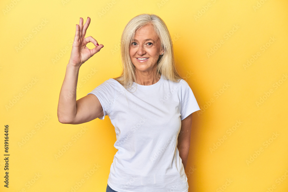 Middle-aged Caucasian woman in white t-shirt, yellow studio cheerful and confident showing ok gesture. Middle-aged Caucasian woman in white t-shirt, yellow studio cheerful and confident showing ok gesture.