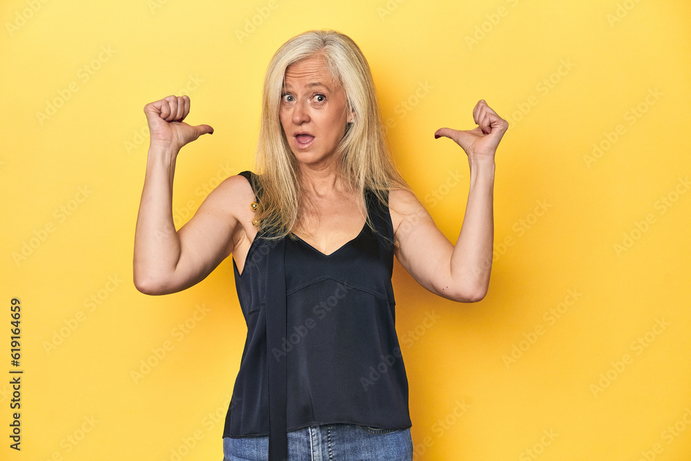 Elegant middle-aged woman in black top, yellow studio feels proud and self confident, example to follow.