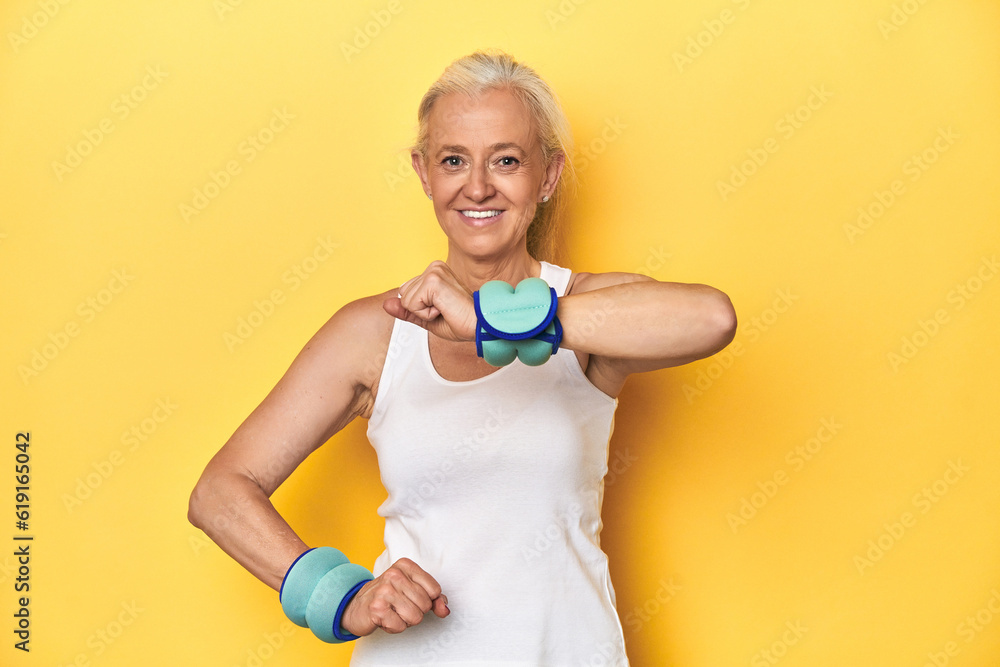 Middle-aged athlete with wrist weights, enhancing workout, yellow background Middle-aged athlete with wrist weights, enhancing workout, yellow background