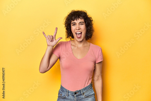 Curly-haired Caucasian woman in pink t-shirt showing a horns gesture as a revolution concept. photo