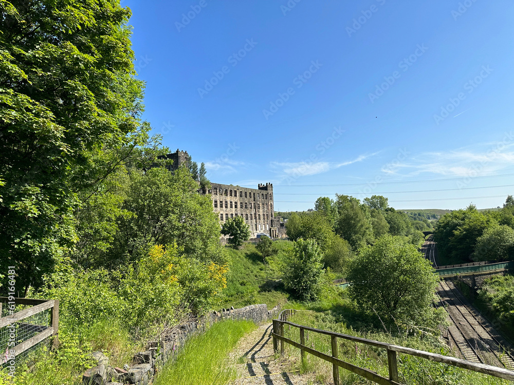 Looking toward a derelict mill, close to the Rochdale train line, with trees, and wild plants in, Littleborough, UK