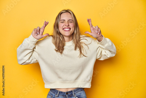 Fotografi Young blonde Caucasian woman in a white sweatshirt on a yellow studio background