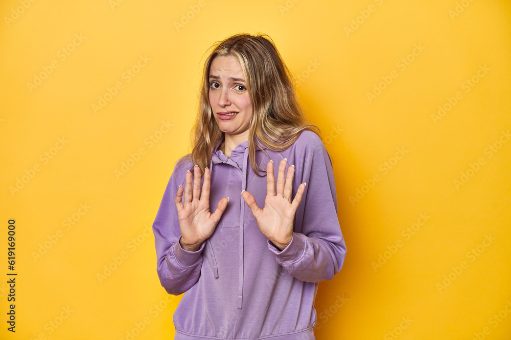 Young blonde Caucasian woman in a violet sweatshirt on a yellow background, rejecting someone showing a gesture of disgust. Young blonde Caucasian woman in a violet sweatshirt on a yellow background, rejecting someone showing a gesture of disgust.