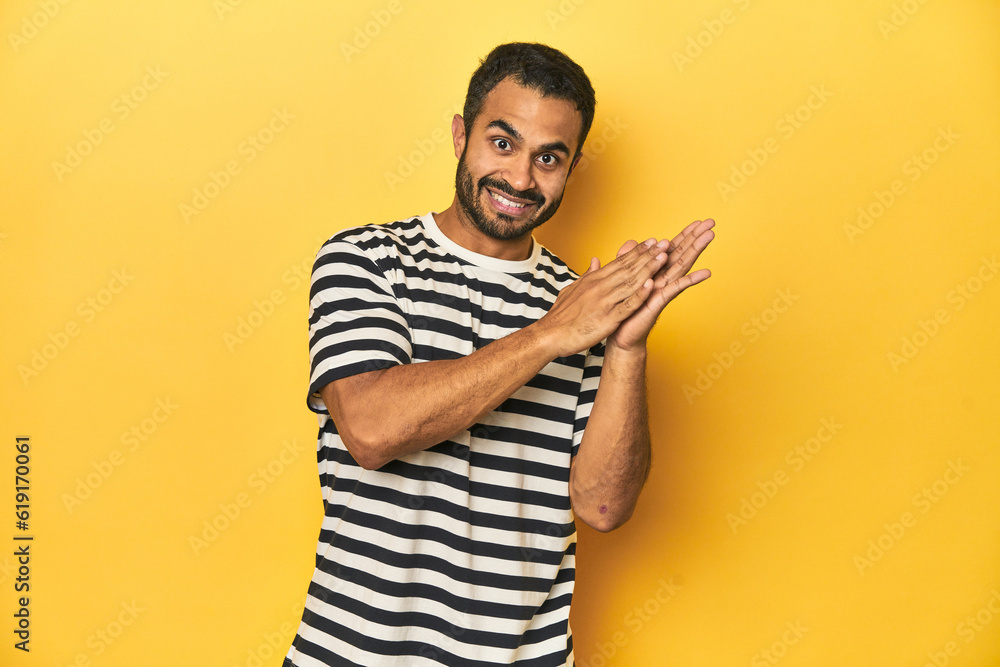 Casual young Latino man against a vibrant yellow studio background, feeling energetic and comfortable, rubbing hands confident. Casual young Latino man against a vibrant yellow studio background, feeling energetic and comfortable, rubbing hands confident.