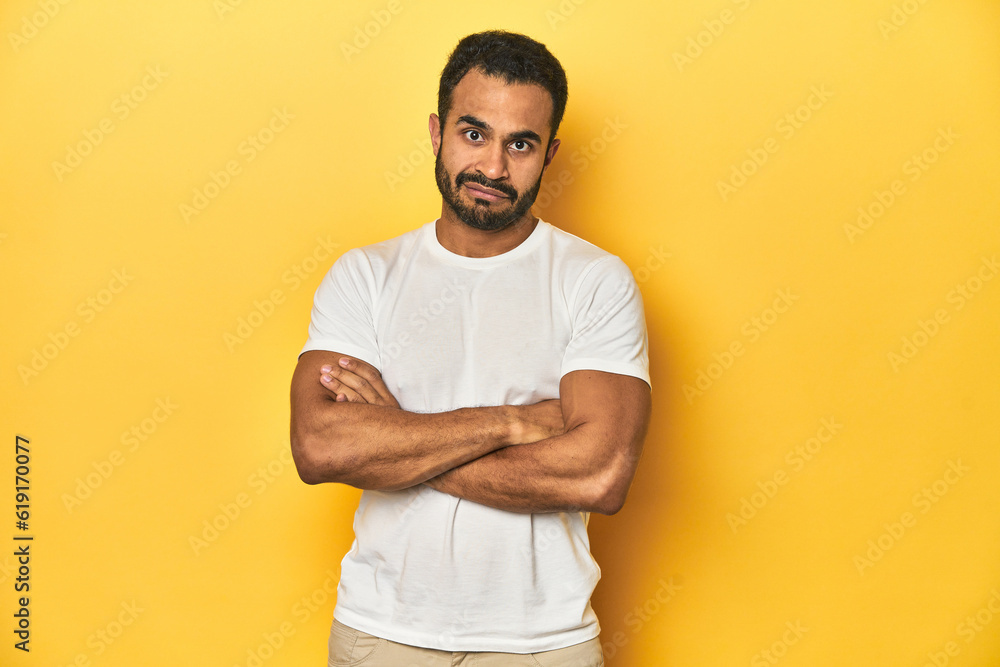 Casual young Latino man against a vibrant yellow studio background, suspicious, uncertain, examining you. Casual young Latino man against a vibrant yellow studio background, suspicious, uncertain, examining you.