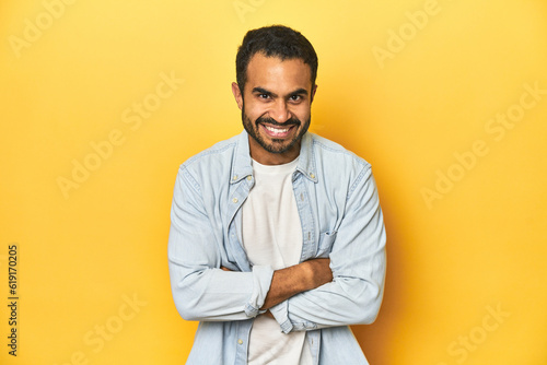Casual young Latino man against a vibrant yellow studio background, laughing and having fun.