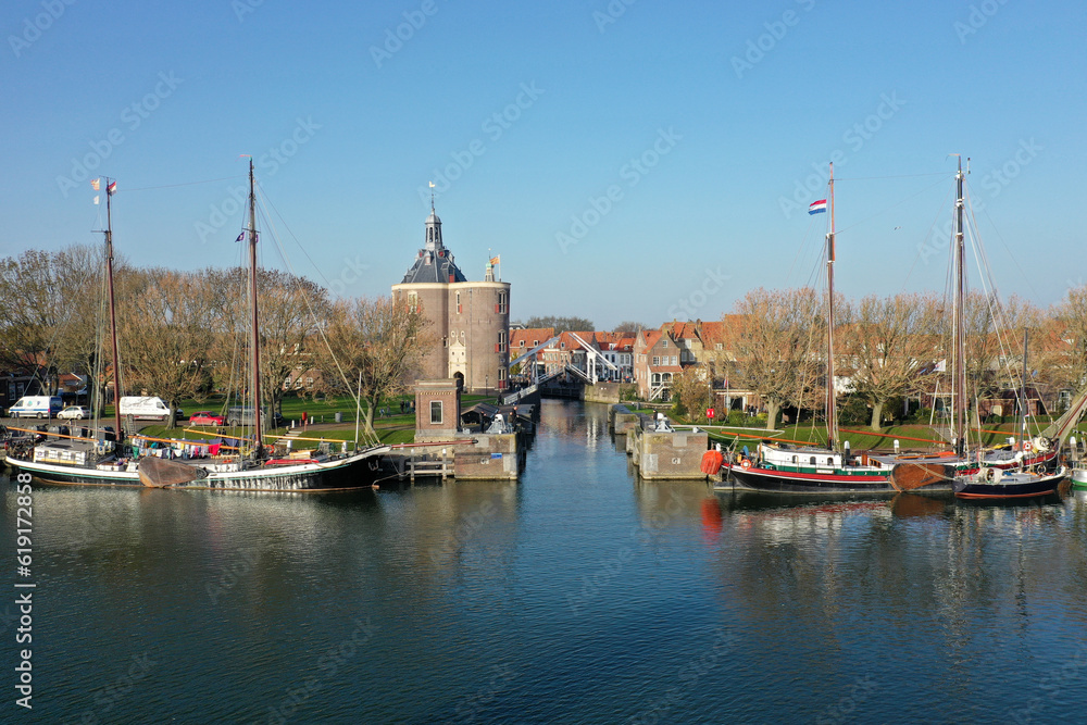 Drone photo of the old lock in Enkhuizen with the drommedaris tower in the background and a wooden sailing boats in the front.