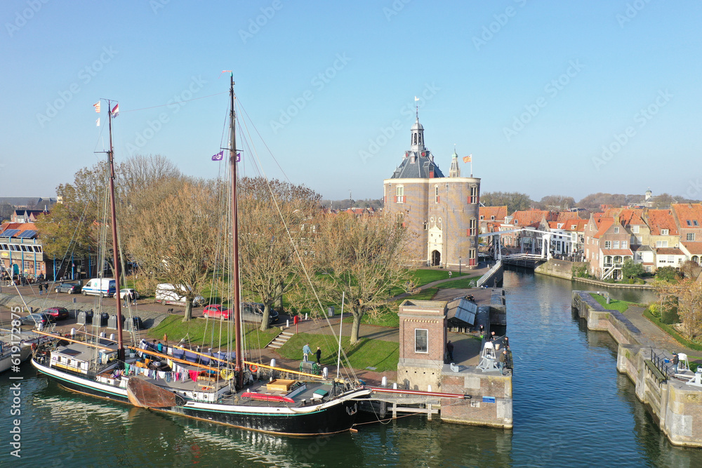  Drone photo of the old lock in Enkhuizen with the drommedaris tower in the background and a wooden sailing boats in the front.