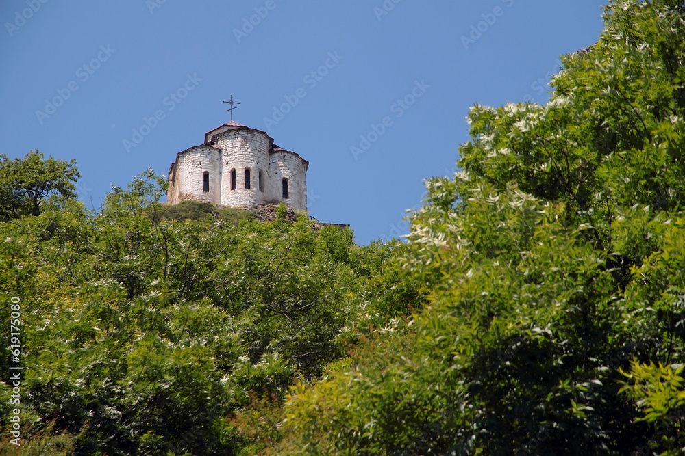 View of an old abandoned ancient temple on a high hill among green trees against a blue sky. Historical architecture, tourism.