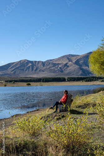 Senior woman rests sitting sunbathing in front of Laguna Zeta, in Esquel, Chubut Argentina.
