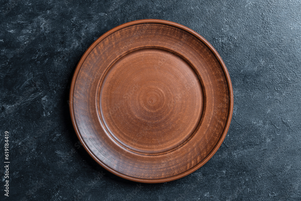 Empty flat plate of red clay over black background . Top view, closeup . Rough ceramic bowl background with copy space Empty flat plate of red clay over black background . Top view, closeup . Rough ceramic bowl background with copy space