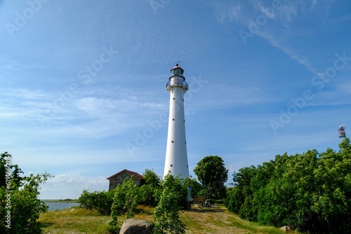 Kihnu island lighthouse in Estonia. Stand alone single white lighthouse stones green forest summer blue sky.