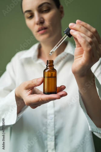 A smiling woman holds a brown bottle of essential oil in her hands and with a pipette.