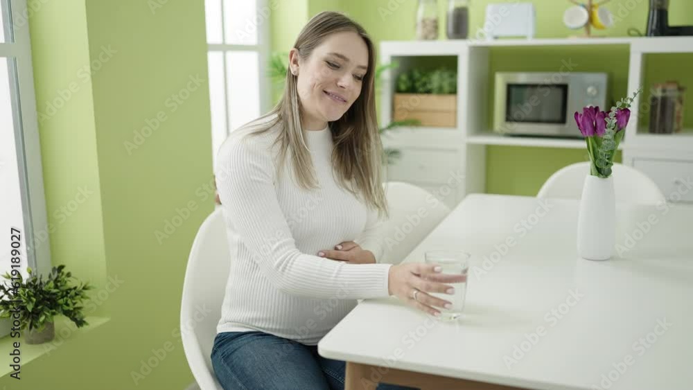 Young pregnant woman drinking glass of water sitting on table at dinning room Young pregnant woman drinking glass of water sitting on table at dinning room
