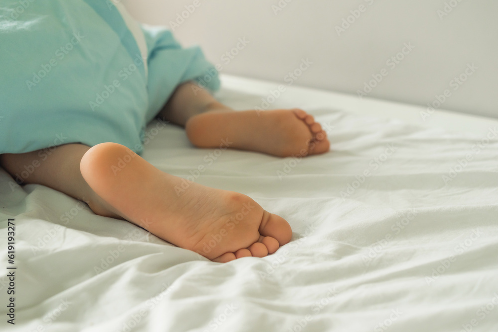 Children's legs stick out from under the blanket. A child's bed with protruding legs. Cute baby heels Children's legs stick out from under the blanket. A child's bed with protruding legs. Cute baby heels