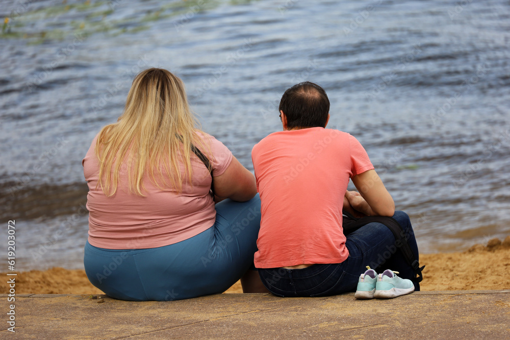 Couple in love sitting on summer beach. Fat woman and slim man, relationship and care