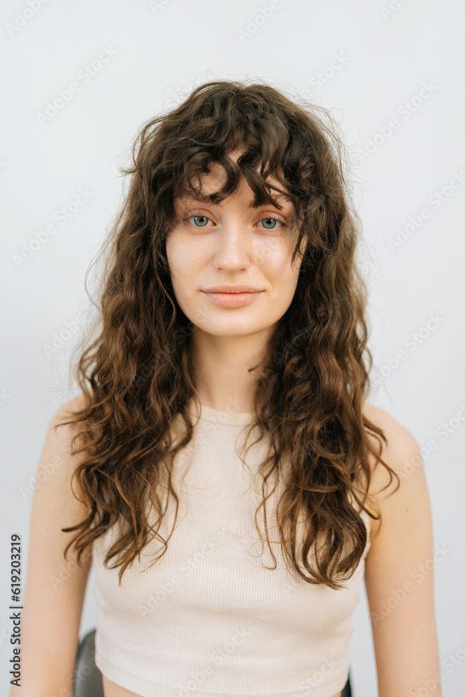 Vertical studio portrait of pretty young woman before applying professional makeup and making stylish hairstyle standing on isolated white background, looking at camera. Concept of fashion and beauty Vertical studio portrait of pretty young woman before applying professional makeup and making stylish hairstyle standing on isolated white background, looking at camera. Concept of fashion and beauty