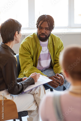 Vertical image of group of people talking to psychologist at session in the room