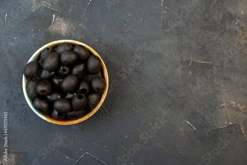 Above view of fresh black olives in a white bowl onthe right side on dark color table with free space photo