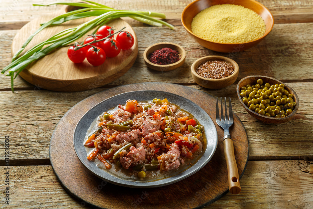 Israeli style couscous with sumac and chicken stew pieces on the table in a plate next to spices and vegetables and couscous grits. Israeli style couscous with sumac and chicken stew pieces on the table in a plate next to spices and vegetables and couscous grits.