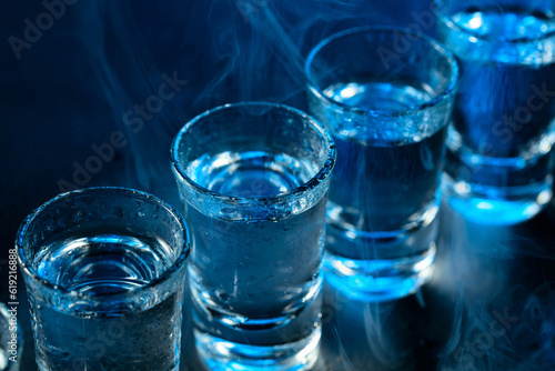 Wet glasses of vodka in smoke on dark blue background. © Igor Normann