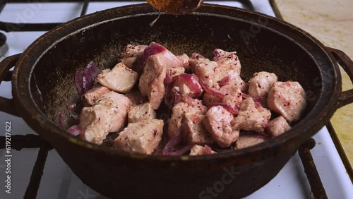 Chicken pieces with red onion and sumac in a pan are mixed with a wooden spatula photo