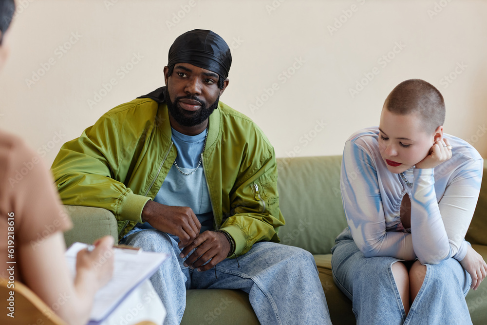 Multiethnic young couple sitting on sofa and listening to psychologist at session