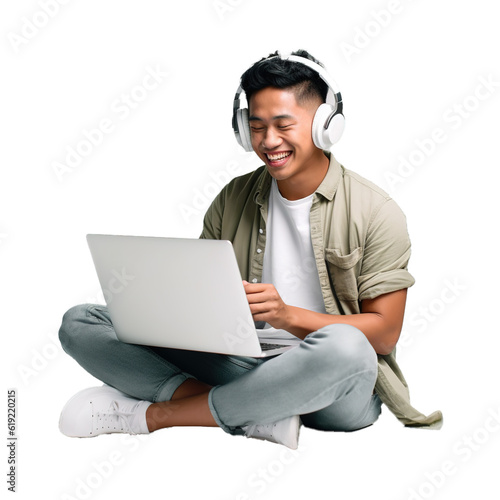 Happy young Asian man sitting on the floor using laptop and wearing headphones photo
