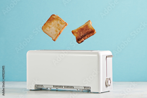 Roasted toast bread popping up of toaster with blue wall, front view