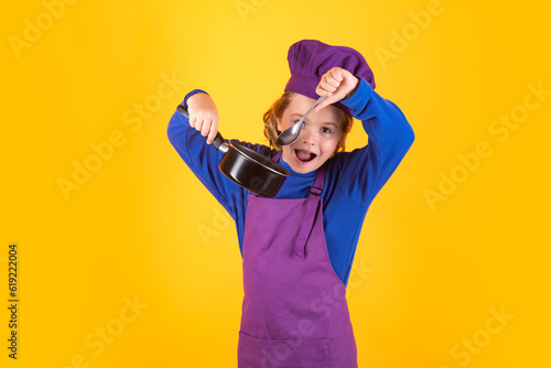 Kid chef cook with cooking pot stockpot. Cooking children. Chef kid boy making healthy food. Portrait of little child in chef hat isolated on studio background. Kid chef. Cooking process. © Olena