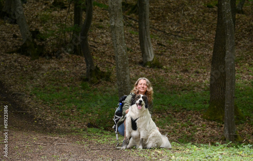 A girl with a white sheperd dog walks in the forest.