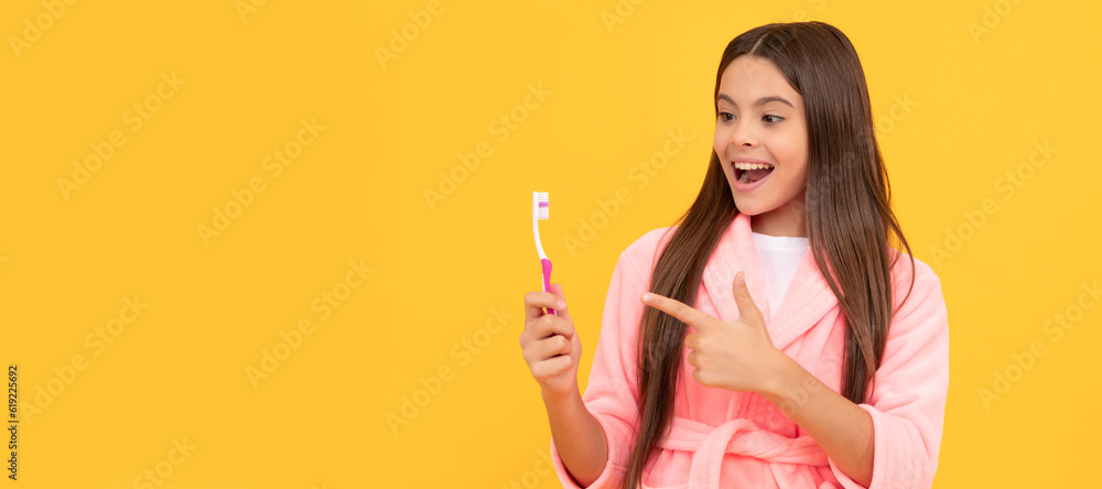 amazed teen girl in home terry bathrobe pointing finger on toothbrush, healthy teeth. Banner of child girl with teeth brush, studio portrait, header with copy space. amazed teen girl in home terry bathrobe pointing finger on toothbrush, healthy teeth. Banner of child girl with teeth brush, studio portrait, header with copy space.