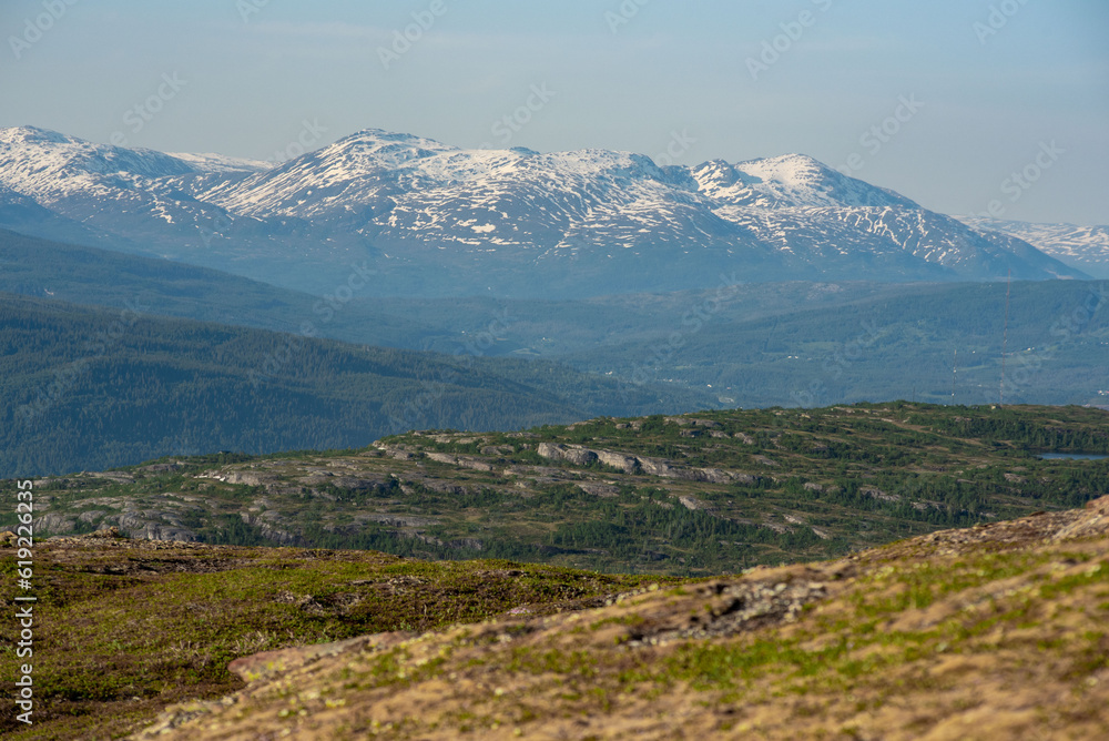 Fototapeta premium View over nordic mountain peaks in Norway from a hike up Hauknestinden, Hauknes, Mo i Rana, Helgeland, Norway. High peaks in a fjord landscape, snow covered. Clear Norwegian summer skies. Wild Norway