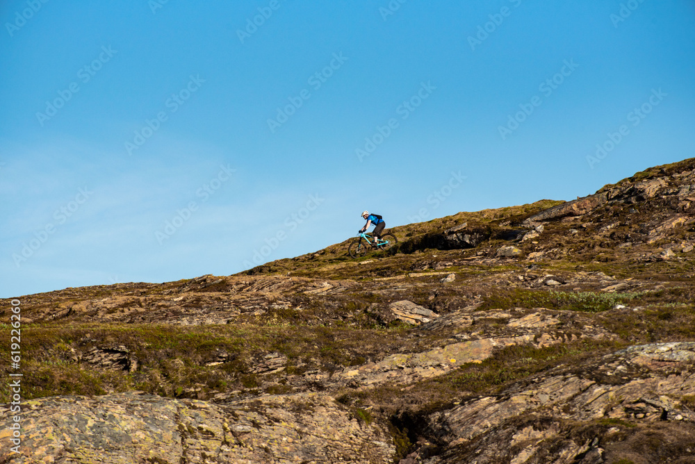 Mountain biker going down the hills of Hauknestinden, Hauknes, Mo i Rana, Helgeland, Norway. Mountainbiking in Norwegian fjell. sunny biking Nordnorge. Biking fast downhill
