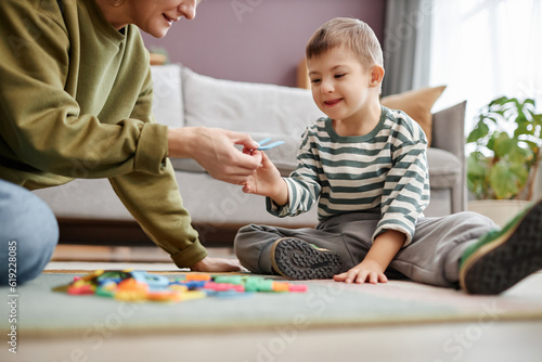 Fototapeta Portrait of happy little boy with down syndrome playing with letters on floor an