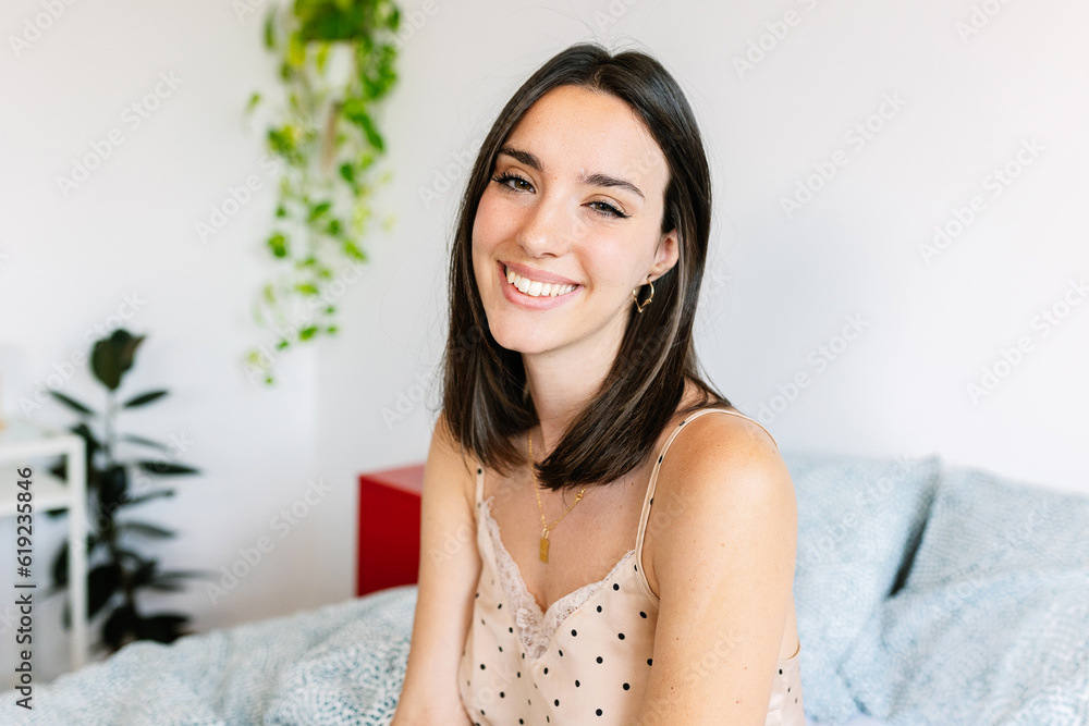 Happy young woman sitting on bed while looking at camera showing toothy smile in the morning. Beautiful people concept. Happy young woman sitting on bed while looking at camera showing toothy smile in the morning. Beautiful people concept.