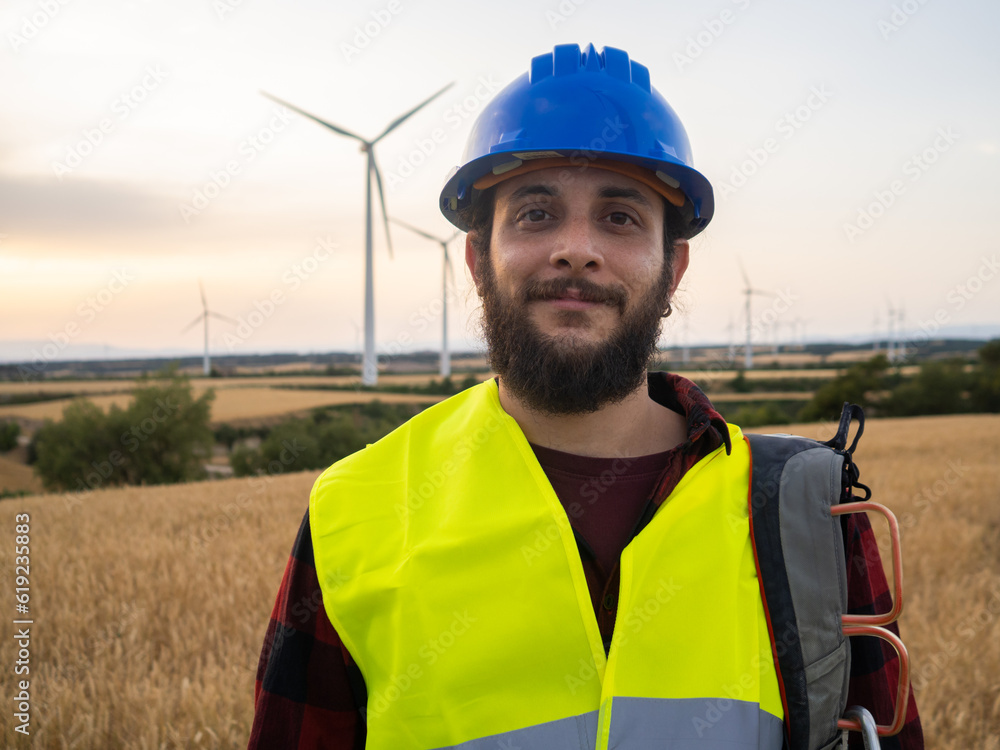 Worker man with helmet looking at camera smiling in a field of windmills